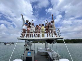 A lively group of friends celebrates on the upper deck of a pontoon boat, enjoying a fun day on the water with drinks and laughter.
