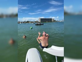A man leaps off a boat into the water while another swims nearby, capturing the essence of fun and adventure on a sunny day out on the water.