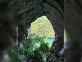 A stunning view from inside a cave, showcasing lush green mountains and tranquil waters beyond — a perfect representation of natural beauty and adventure.