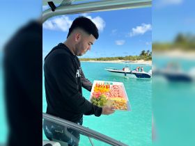 A man presents a colorful platter of fruits and snacks aboard a boat, perfect for enjoying a delightful meal while cruising in the turquoise waters.