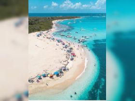 A vibrant scene at a sandy beach with numerous boats anchored nearby, showcasing a lively atmosphere of swimming and relaxation — perfect for a day of fun in the sun.