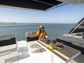 A woman enjoys a leisurely breakfast on the deck of a stylish boat, complete with fresh fruit and drinks, perfect for a relaxing day on the water.