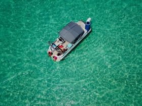 A lively group enjoys a day on a pontoon boat in crystal-clear turquoise waters, perfect for swimming and relaxation.