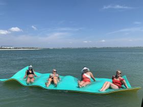 A group of friends enjoys a sunny day on a floating mat in the water, perfect for relaxation and fun under the sun.