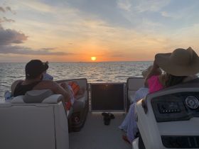 A serene sunset view from a pontoon boat, where a couple enjoys a relaxing moment on the water, making it a perfect backdrop for romantic outings or family gatherings.