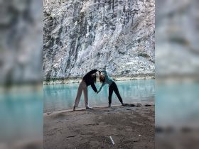 Two friends pose joyfully against a stunning rocky backdrop by the water, capturing a memorable moment during their adventure.