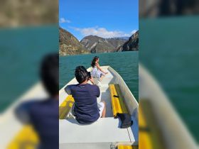 A couple enjoys a picturesque boat ride, capturing memories against a stunning backdrop of mountains and clear waters.