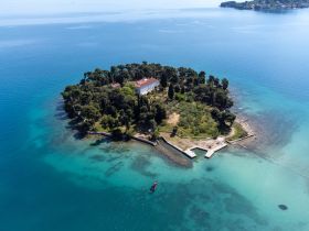 A stunning aerial view of a secluded island surrounded by crystal-clear waters, showcasing lush greenery and a charming building — an ideal destination for tranquil getaways and exploration.