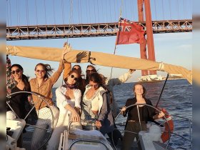A joyful group of friends celebrates aboard a sailboat, enjoying the sunset and the scenic backdrop of a bridge — perfect for memorable sailing adventures.