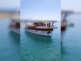 A lively group celebrates aboard the 'Nera' boat, enjoying a sunny day on the water with a beautiful beach backdrop.