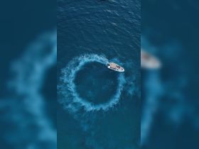 An aerial view captures a speedboat making a thrilling turn in the vibrant blue waters, showcasing the excitement of on-water activities.