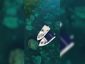 Aerial view of two boats with a group of people enjoying the sun and water, showcasing a perfect day out on the crystal-clear sea.
