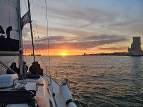 A group enjoys a stunning sunset while sailing, with a picturesque harbor backdrop — perfect for memorable sailing experiences.