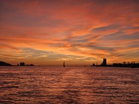 A stunning sunset over the water with a sailboat silhouetted against the vibrant sky, capturing the beauty of coastal evenings.