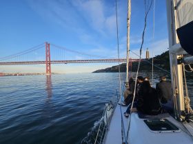 A group enjoys a scenic sailing experience near the iconic red bridge in Lisbon, capturing the beauty of the city from the water.