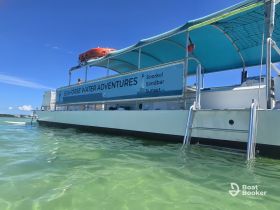 A close-up view of the Seahorse Water Adventures boat, featuring a vibrant blue canopy and signage for snorkeling and sunset tours, anchored in clear waters.