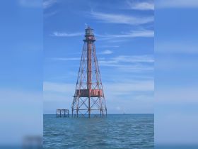 A lighthouse stands prominently in the water against a blue sky, showcasing a scenic maritime landmark.
