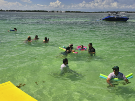 A lively group enjoys a fun day in the water, engaging in swimming and water activities, with a boat visible in the background — perfect for summer outings and family adventures.