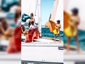 A lively group enjoys a sailing adventure, playfully waving colorful fabrics on the deck — perfect for summer fun and memorable experiences on the water.