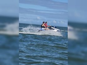 Two friends enjoy an exhilarating ride on a jet ski, creating splashes as they speed across the water — a perfect adventure for thrill-seekers.