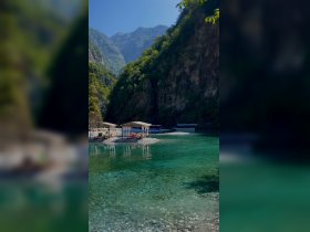 A stunning view of a serene bay surrounded by towering cliffs and lush greenery, featuring colorful beach loungers on a pebbled shore — an ideal destination for relaxation and exploration.