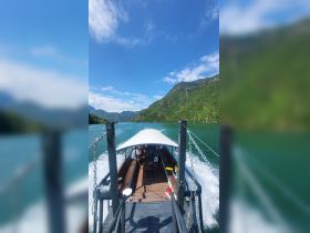 A scenic view from the back of a boat cruising along a river, surrounded by lush mountains — perfect for exploring nature and enjoying outdoor adventures.