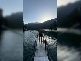 A person stands on a dock overlooking serene waters and majestic mountains at sunset, capturing the essence of a tranquil getaway.