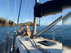 Two friends enjoy a serene moment on the deck of a sailboat, overlooking stunning coastal scenery — a perfect escape for sailing enthusiasts.
