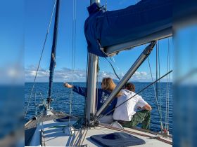 Two individuals enjoy a scenic sailing experience, pointing towards the horizon while relaxing on the deck of their boat — a perfect moment for ocean lovers.