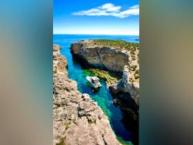 A stunning aerial view of a boat navigating through a narrow channel, surrounded by rocky cliffs and crystal-clear waters, perfect for exploring hidden coves.