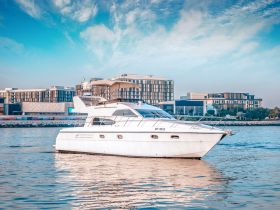 A stunning yacht glides through calm waters, showcasing its elegant design against a backdrop of modern buildings — perfect for luxury outings and charters.