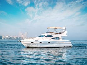 A stunning side view of a yacht cruising through calm waters, showcasing its elegant design against a backdrop of modern buildings and a clear blue sky.