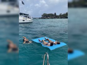 A group enjoys a fun day on the water, with two relaxing on a floating mat and one snorkeling nearby, showcasing the perfect tropical getaway.