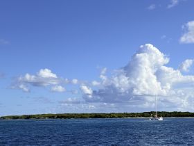 A serene view of a sailboat anchored near a lush island, surrounded by clear turquoise waters and a bright blue sky — perfect for showcasing tranquil boating experiences.