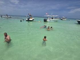 A lively scene at a beach with families enjoying the water, showcasing a fun day of swimming and relaxation among several boats.