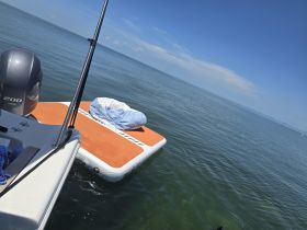 A floating mat is anchored beside a boat in calm waters, perfect for relaxing and enjoying the sun while out on the water.