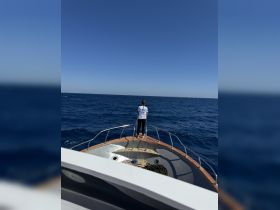 A person stands at the bow of a boat, enjoying the expansive ocean view under a clear blue sky — a perfect moment for adventure on the water.