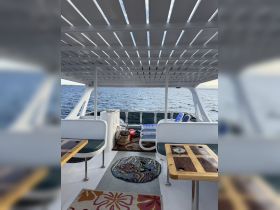 Interior view of a boat's lounge area featuring comfortable seating and a vibrant rug, perfect for relaxing while enjoying the scenic ocean views.