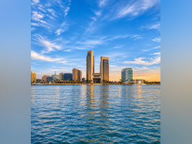A scenic view of a city skyline reflecting on the water, showcasing modern architecture against a vibrant sky.
