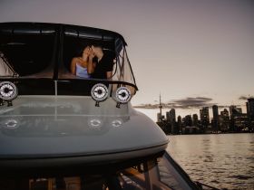 A couple shares a romantic kiss on a boat at sunset, with a stunning city skyline in the background — perfect for intimate moments on the water.