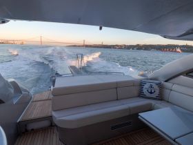 A cozy interior view of a yacht showcasing comfortable seating and a scenic backdrop of the water and bridge, perfect for relaxing during a cruise.