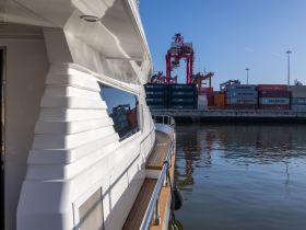 A close-up view of a sleek yacht's exterior, showcasing its design against a backdrop of shipping containers at the dock — perfect for maritime enthusiasts.