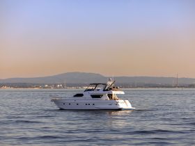 A stunning yacht glides through calm waters, showcasing its elegant design against a serene backdrop of mountains and a hazy sky.