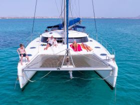 A family enjoys a sunny day on a catamaran, with kids playing and adults relaxing on the deck — a perfect setting for summer adventures on the water.