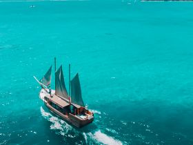 A stunning aerial view of a sailboat navigating through crystal-clear turquoise waters, showcasing the beauty of sailing adventures.