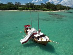 A vibrant scene featuring a boat with a water slide, where guests enjoy swimming in the turquoise waters — perfect for a fun-filled day on the water.