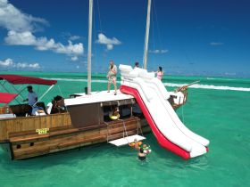 A lively scene on a boat featuring a water slide, with guests enjoying swimming and fun in the vibrant turquoise waters — perfect for family adventures and group outings.