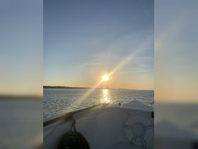 A serene sunset view from the bow of a boat, showcasing the tranquil waters and the fading light — perfect for evening cruises.