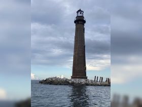 A tall lighthouse stands on a rocky shore under a cloudy sky, providing a scenic backdrop for maritime adventures.