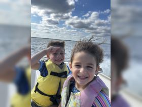 Two children enjoy a fun day on the water, smiling and wearing life jackets while riding on a boat — a perfect moment of joy and adventure.